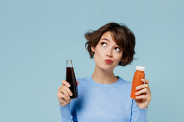 Young minded woman 20s wear casual sweater hold soda cola water vegetable smoothie choose between...