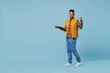 Naklejka premium Full size body length young black man 20s years old wear yellow waistcoat shirt hold use work on laptop pc computer doing winner gesture isolated on plain pastel light blue background studio portrait
