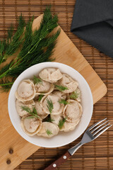 Dumplings in a white plate, with dill on a wooden board