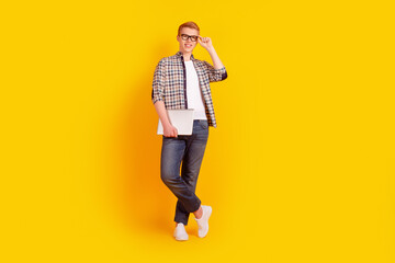 Full body photo of young cheerful guy hand touch eyeglasses hold laptop isolated over yellow color...