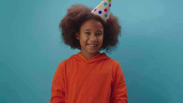 Smiling African American girl receives birthday gift standing on blue background. Kid is happy to get birthday present.