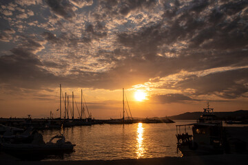 Fototapeta na wymiar Beautiful scene of sunset over harbour in small fishing village at sea in Nea Skioni, Greece. Greek marina with sillhouetes of parked boats and yachts.