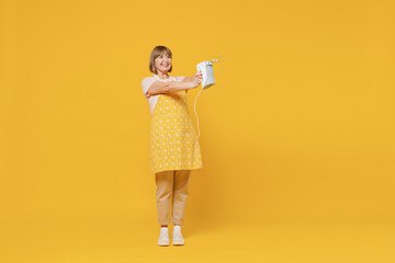 Full body elderly happy cheerful satisfied housekeeper housewife woman 50s in orange apron holding mixer cooking isolated plain on yellow background studio portrait People household lifestyle concept