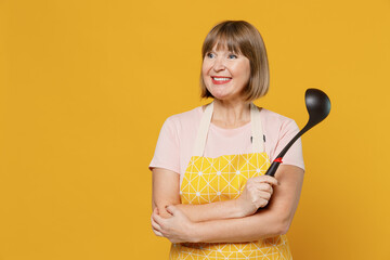 Elderly smiling happy fun housekeeper housewife woman 50s in orange apron hold ladle look aside on...