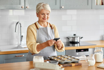 cooking, food and culinary concept - happy smiling senior woman with smartphone taking picture of...