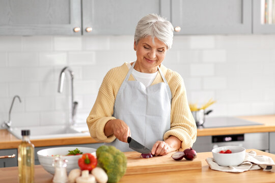 Healthy Eating, Food Cooking And Culinary Concept - Happy Smiling Senior Woman With Knife Chopping Red Onion On Kitchen At Home