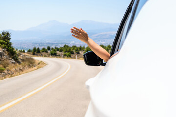 Woman sticking hand out from the open window driving a car. Trip on the serpentine road in the mountains. Summer vacation. Freedom concept. copy space