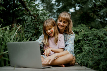 Mother with child are playing on laptop in the garden