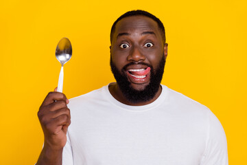 Photo of funny positive handsome guy hold spoon tongue lick teeth lips isolated on yellow color...
