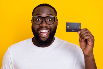 Portrait of impressed astonished person hold demonstrate debit plastic card isolated on yellow color background