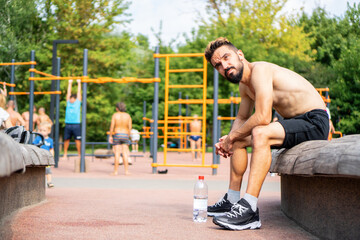 Sportive brunette man with beard sits at the training sportground.