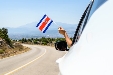 Woman holding Costa Rica flag from the open car window driving along the serpentine road in the mountains. Concept