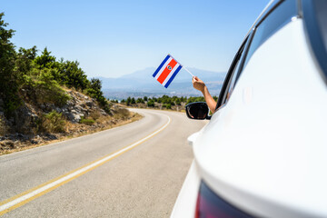 Woman holding Costa Rica flag from the open car window driving along the serpentine road in the mountains. Concept - 473295156