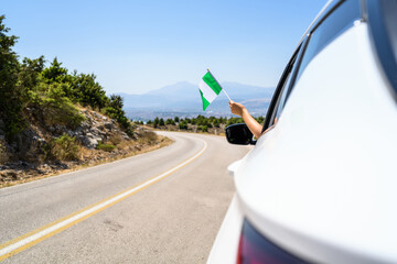 Woman holding Nigeria flag from the open car window driving along the serpentine road in the...
