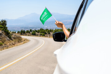 Woman holding Saudi Arabia flag from the open car window driving along the serpentine road in the...