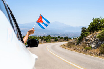 Woman holding Cuba flag from the open car window driving along the serpentine road in the mountains. Concept