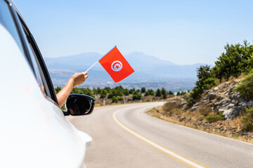 Woman holding Tunisia flag from the open car window driving along the serpentine road in the...