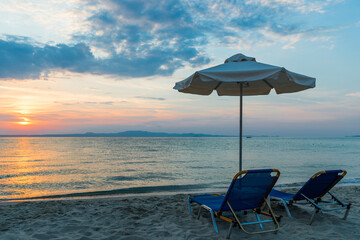Beautiful sunset seascape with beach chairs and umbrella on the coast, Greece