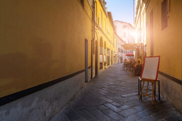 Fototapeta na wymiar Lucca, Tuscany, Italy. August 2020. In an alley in the historic center, the tables of a restaurant with seated customers. Street paved with stones, the colorful facades of the houses frame it.