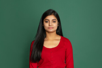 Obraz premium Half-length portrait of young beautiful smiling girl, student looking at camera isolated on dark green studio backgroud