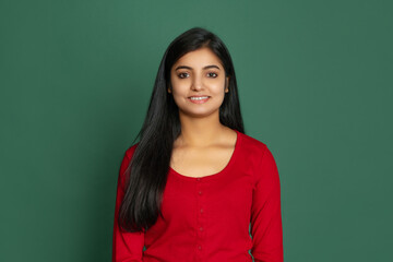 Fototapeta premium Half-length portrait of young beautiful smiling girl, student looking at camera isolated on dark green studio backgroud