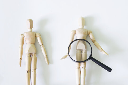 Wooden figurines of people and a magnifying glass on a white background. The concept of gender identification and self-identification. Anatomy study concept. Third gender concept