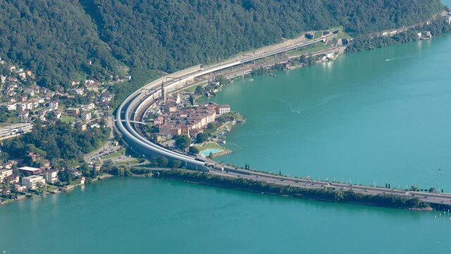 Timelapse, aerial view on cars and trains traffic in Swiss Alpine town near lake. Melide causeway, Bissone, Lake Lugano, Canton Ticino, Switzerland