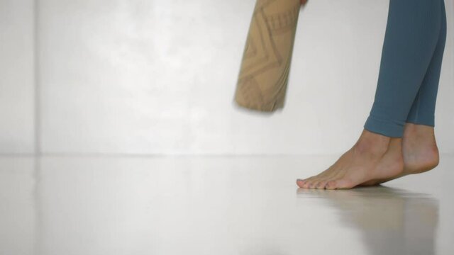 European girl winds up a yoga mat in a white bright room at home. Do sports at home alone.
