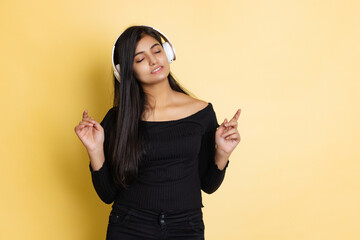 Emotional young adorable cute girl, student in black blouse listening to music in headphones isolated on yellow color studio backgroud