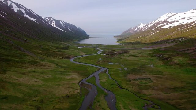 Aerial shot in Iceland flying through a valley surrounded by snowy mountains in Iceland. Slightly overcast.