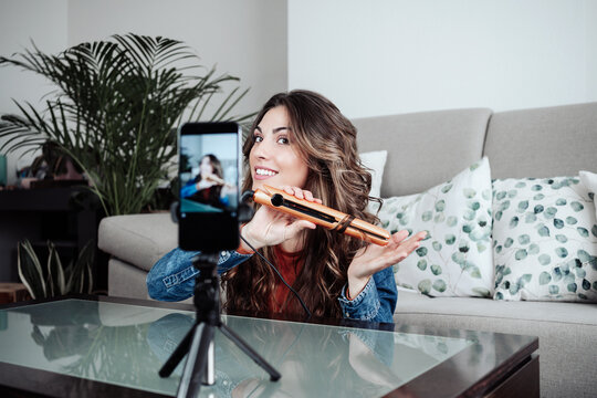 Young vlogger filming tutorial with hair straightener at home