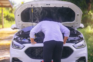 A broken down car, engine open and smoking, serious driver looking at the engine and do nothing....