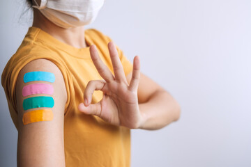 woman showing OK sign with bandage after receiving covid 19 vaccine. Vaccination, herd immunity, side effect, booster dose, vaccine passport and Coronavirus pandemic