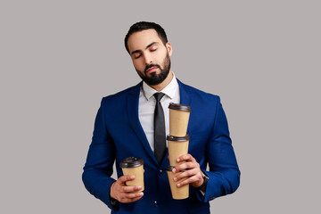 Tired exhausted businessman coffee cups and sleeping, feeling exhausted bored after stressful working day, wearing official style suit. Indoor studio shot isolated on gray background.