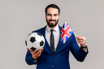 Optimistic smiling man holding hands flag of United Kingdom and football ball, supporting favourite...