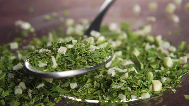 Spicy seasoning with dried chopped crushed garlic and parsley in metallic spoon. Macro. Rotation