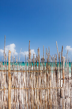 A stick fence along a white sand beach