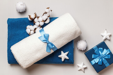 White and blue terry towels with a bow on a gray background. Gift box cotton branch with Christmas...