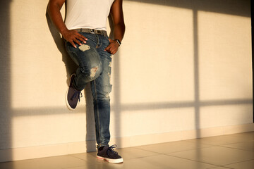 Cool black man in jeans and a white T-shirt stands in the sunlight opposite the window