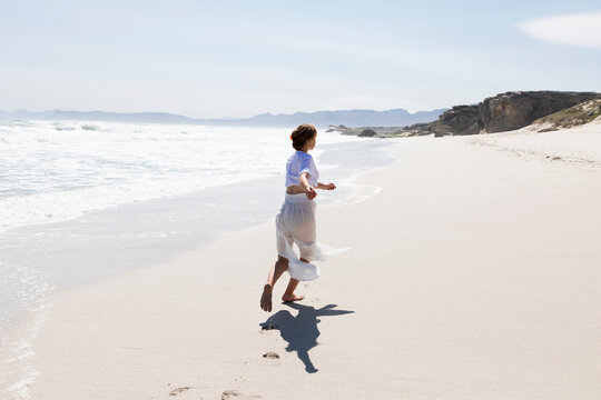 Teenage girl dancing alone on a sandy beach in South Africa by the water's edge