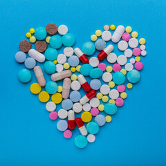 A lot of pills in a heart shape on a blue background as a symbol of treatment to protect the heart. Cardiac disease therapy with free space for text.