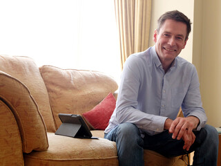 Man sitting on sofa smiling at camera.