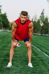 Cheerful sporty man in the park on green grass doing exercises