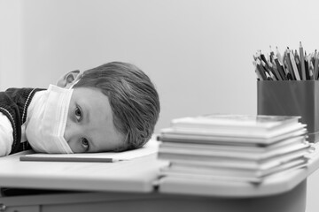 A cute first grader boy in a school uniform at his desk wearing a protective medical mask during the coronavirus pandemic. Selective focus. Close-up. Portrait