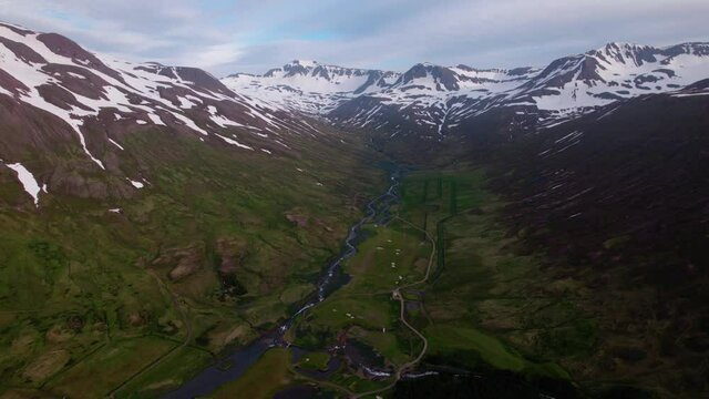 Icelandic aerial in epic mountain landscape. Snowy mountains with lush green valley below. Winding river and road. 