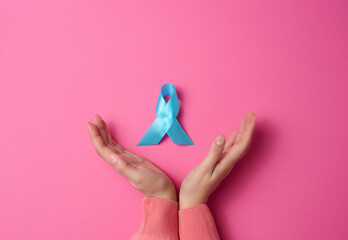 woman hands holding light blue ribbon awareness on a pink background. Men's health and prostate cancer awareness campaign concept.