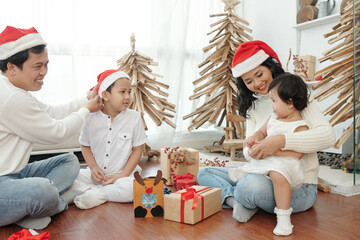 Happy mother, father, son and daughter sitting on the floor and opening Christmas presents