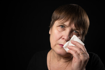 Grandmother with a napkin in her hands is crying on a black background.