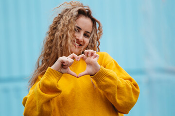 Smiling blond curly haired woman showing heart sign