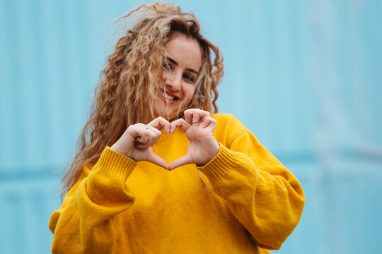 Smiling blond curly haired woman showing heart sign